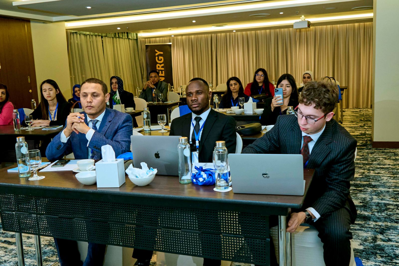 Delegates seated at conference tables with laptops during a session