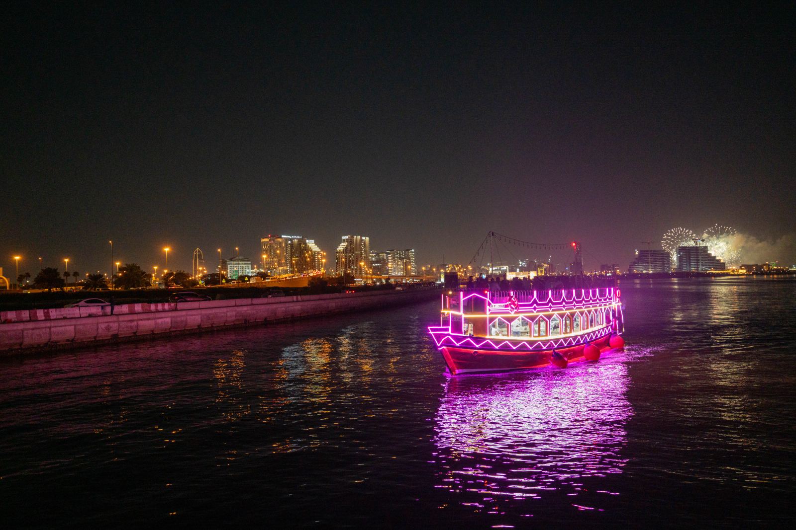 An illuminated traditional dhow boat on Dubai Creek at night
