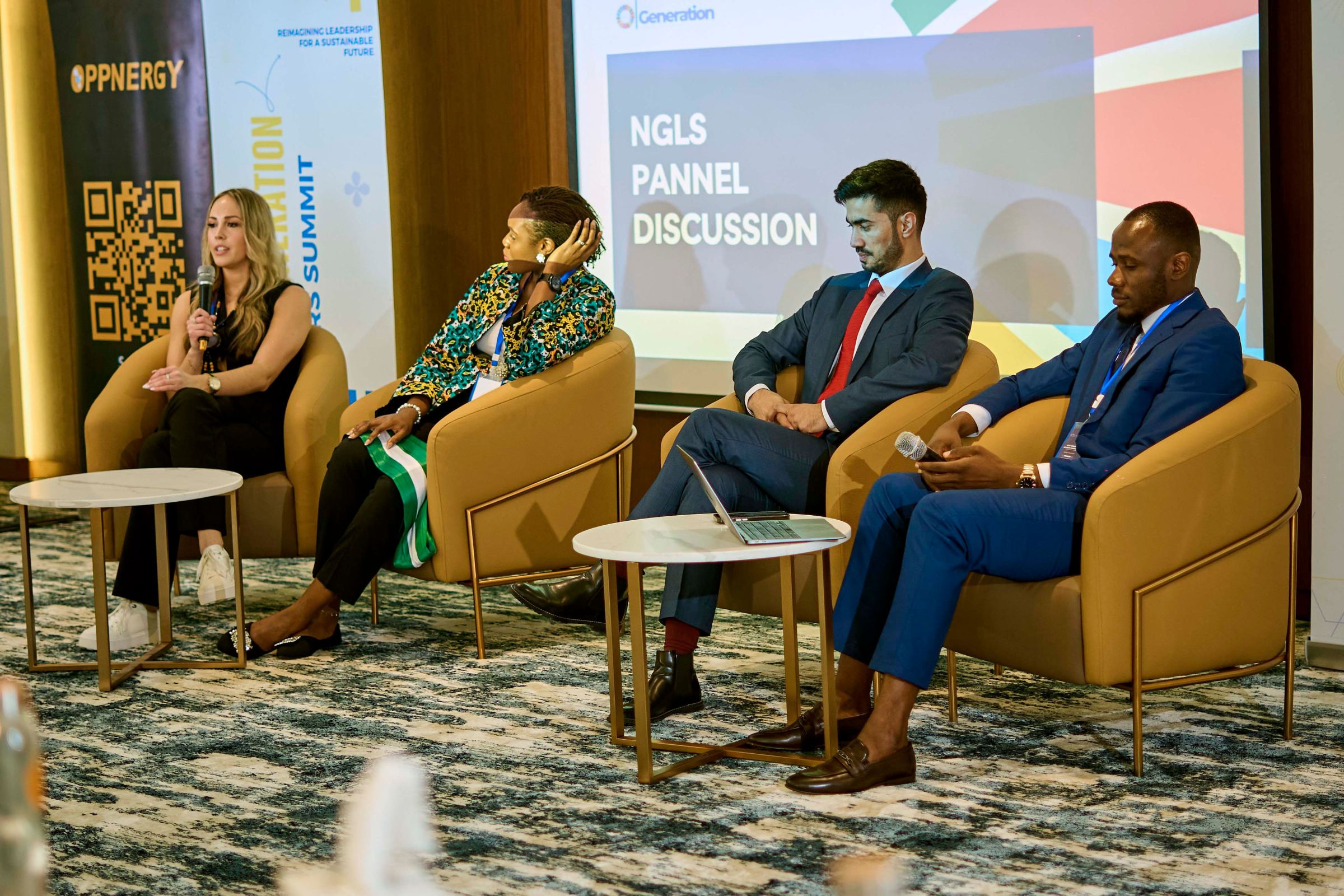 Four panellists in conversation on stage beneath a screen reading NGLS Panel Discussion
