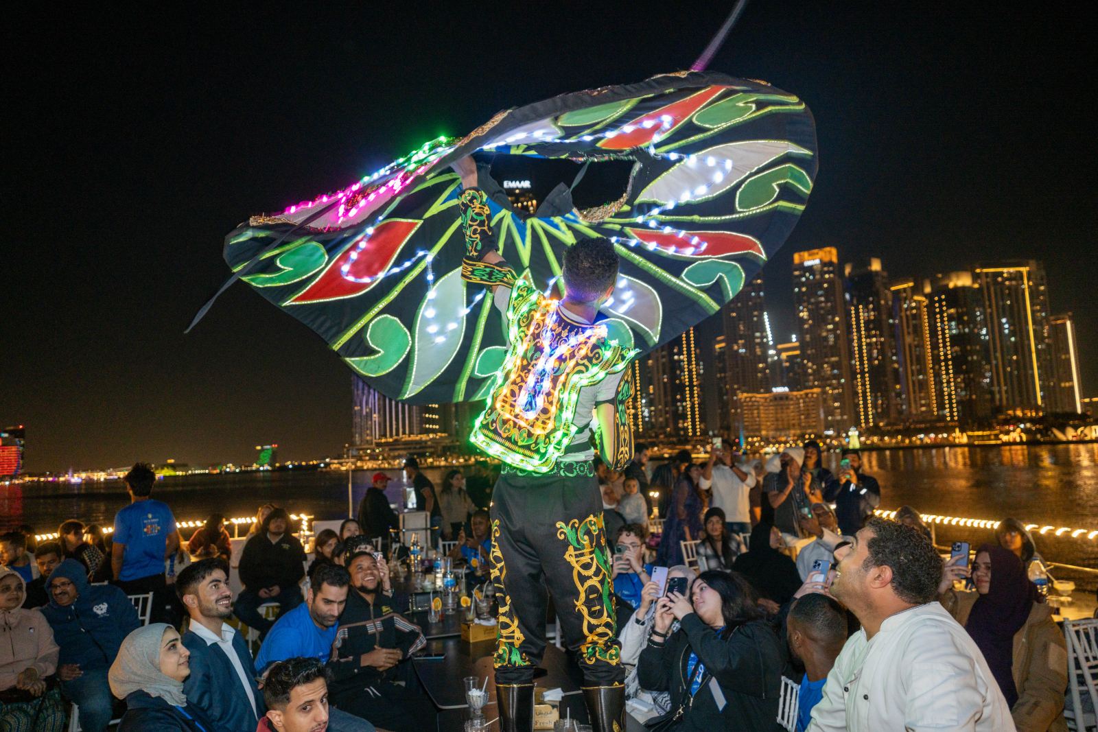 A Tanoura dancer in a glowing costume spinning in front of delegates at night